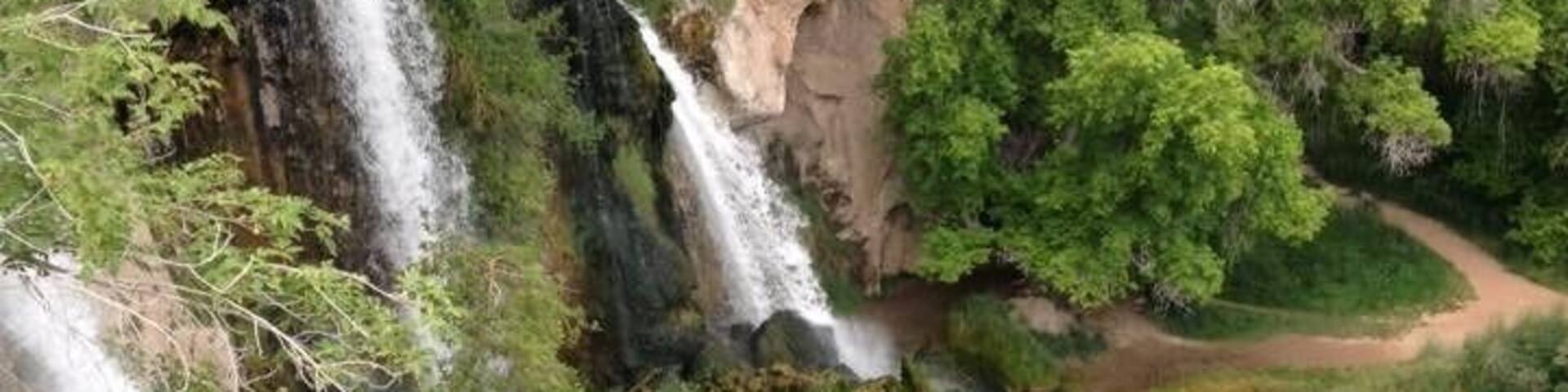 A multi-tiered waterfall surrounded by lush greenery and rocky terrain.
