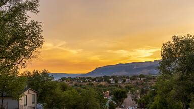 A suburban street with houses, cars, and a mountain range in the background during sunset.