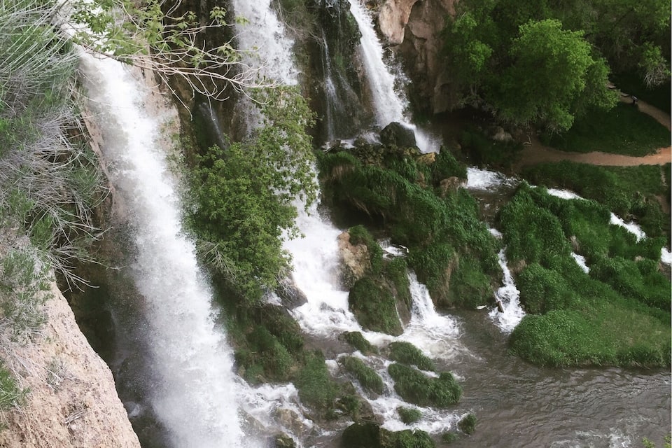 A waterfall cascading down a rocky cliff surrounded by lush greenery.