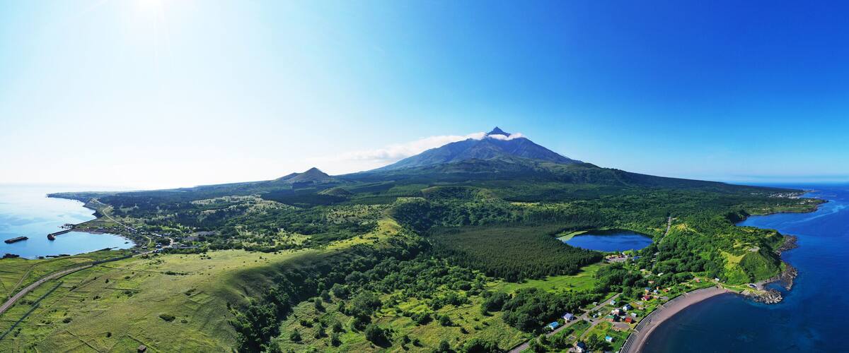 A volcanic mountain with a lake and coastal village.