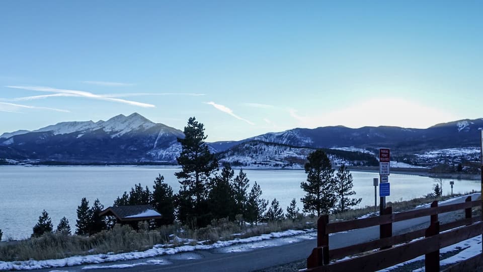 A snow-covered lake with mountains in the background and a wooden fence in the foreground.