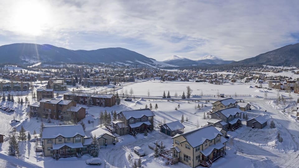 A snow-covered town with buildings, a ski resort, and mountains in the background.