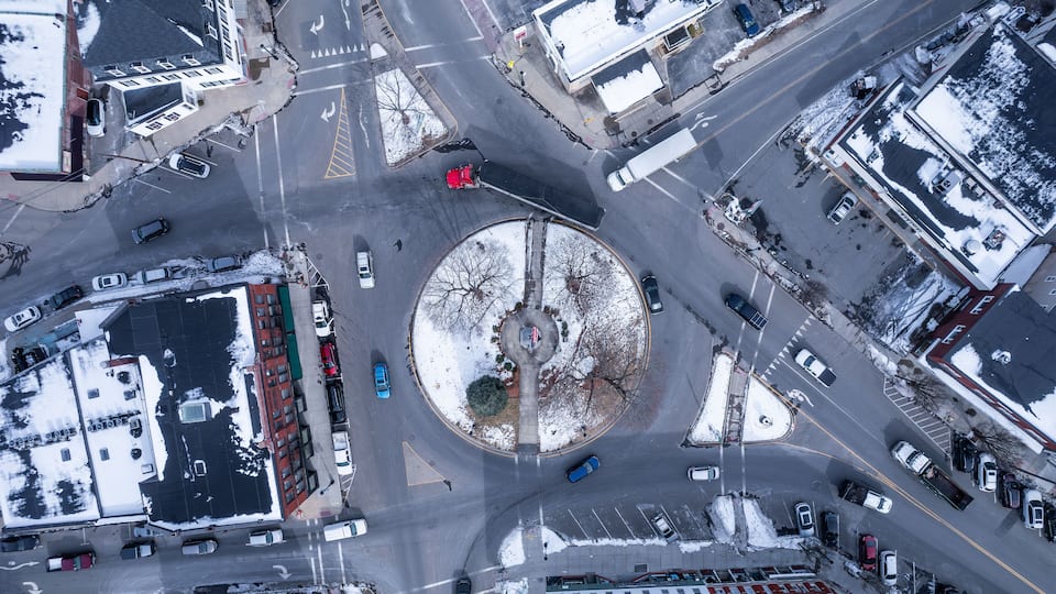 An aerial view of a roundabout with cars, buildings, and snow-covered ground.