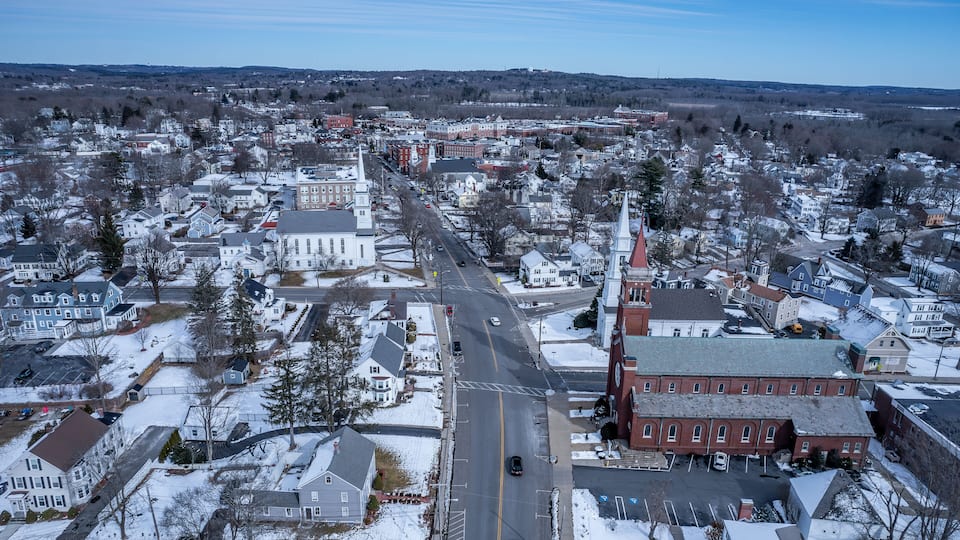 A snow-covered town with a prominent church steeple, a main road, and residential houses.