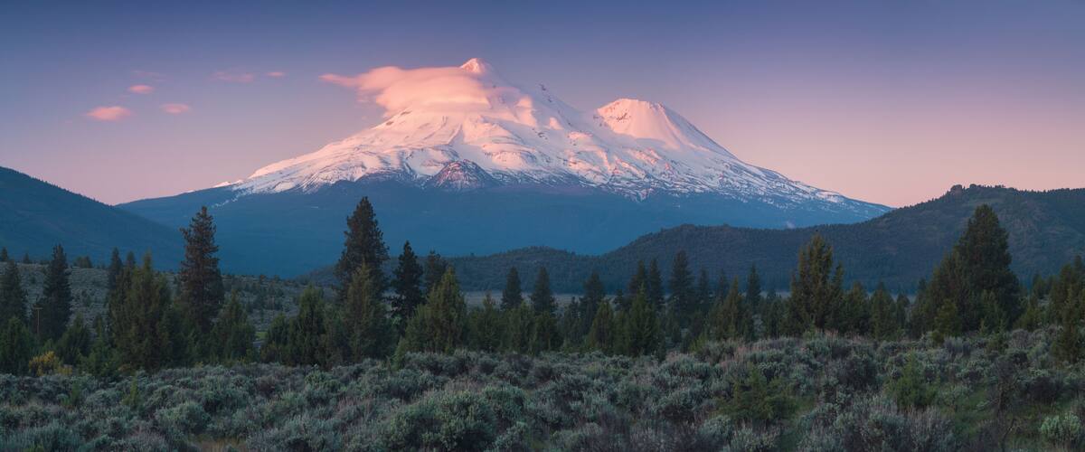 A snow-capped mountain, a forested valley, and a clear sky.