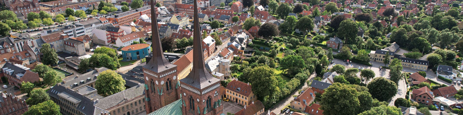 An aerial view of a town with a prominent church featuring a tall spire and a dome, surrounded by residential houses and greenery.