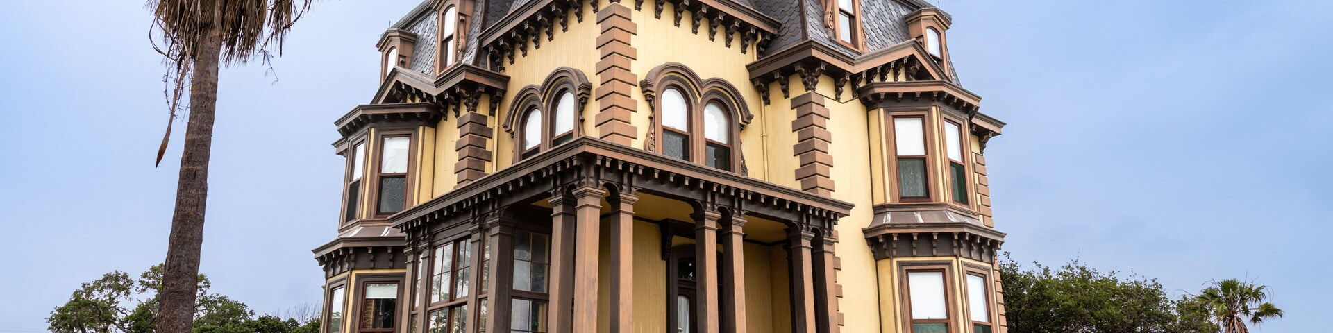 Un edificio histórico con arquitectura ornamentada, una escalera destacada y una palmera en primer plano.