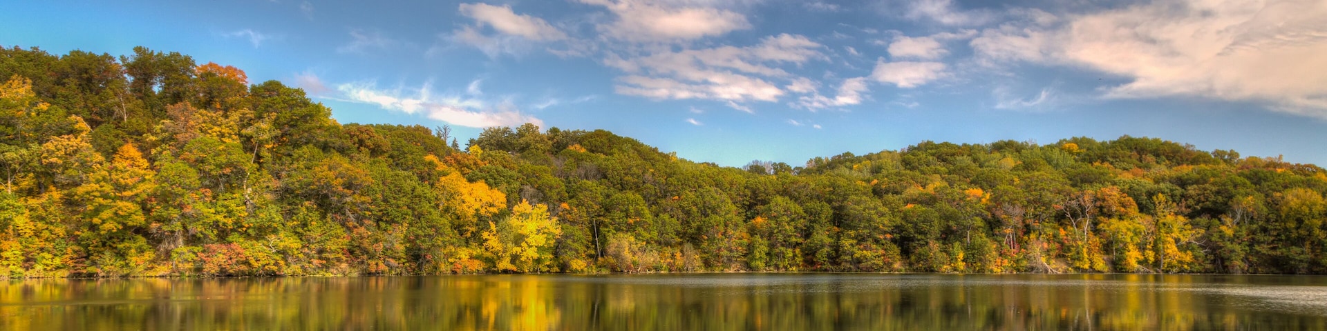Un lago tranquilo que refleja el follaje otoñal y un cielo despejado.
