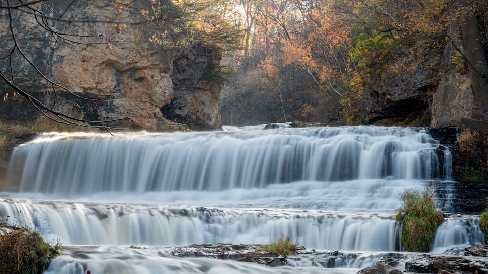A multi-tiered waterfall surrounded by rocky cliffs and autumn foliage.