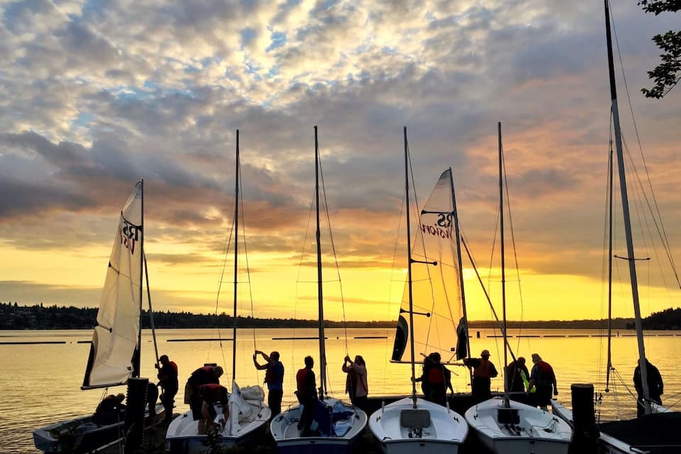 Un grupo de veleros amarrados en un puerto deportivo, con un atardecer de fondo.