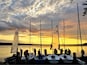 A group of sailboats docked at a marina with a sunset in the background.