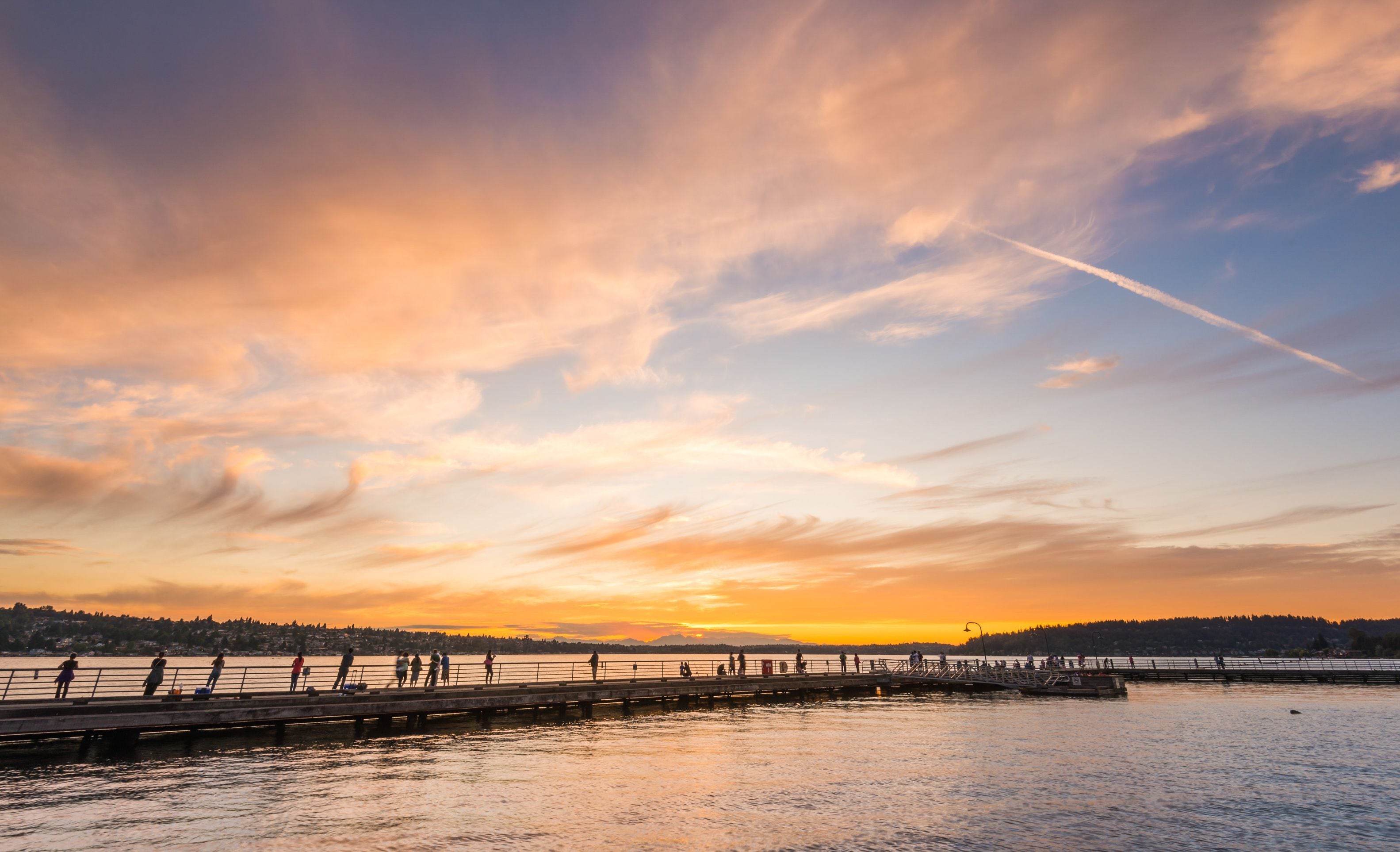 A sunset over a body of water with a pier and people walking.