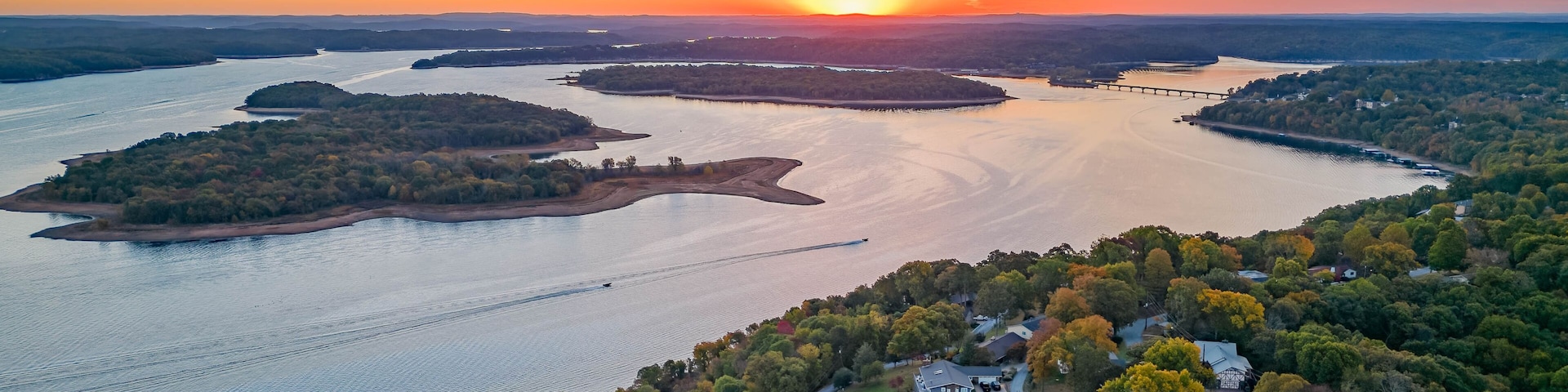 Atardecer sobre un río con islas, rodeado de un bosque denso y zonas residenciales.