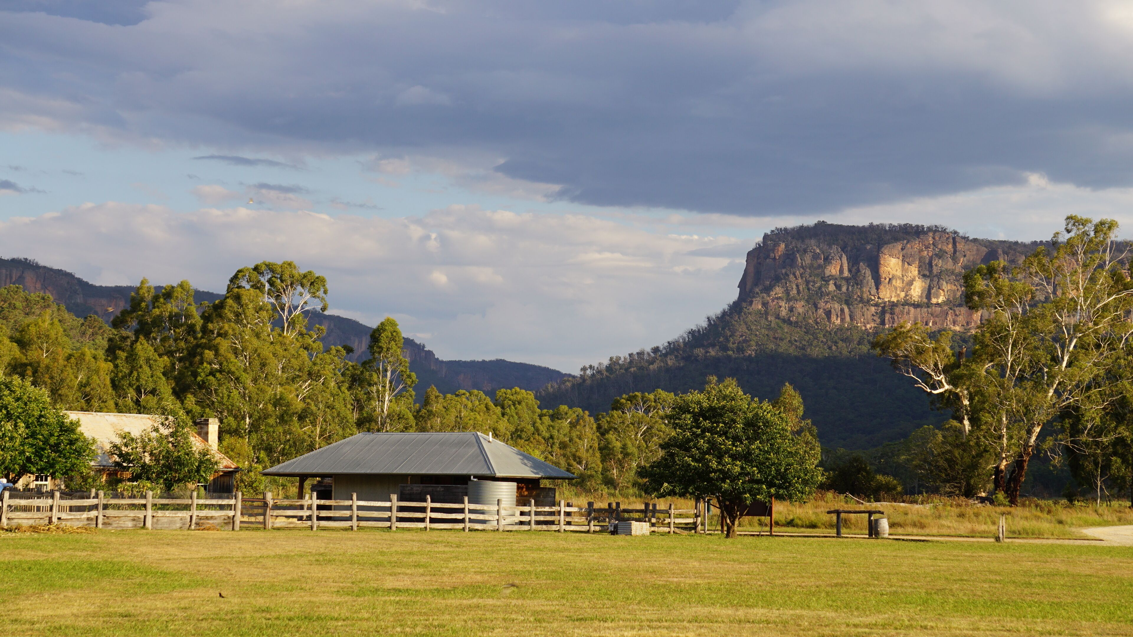 A rural landscape with a barn, trees, and a prominent mountain in the background.