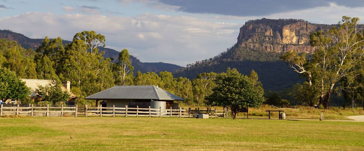 A rural landscape with a barn, trees, and a prominent mountain in the background.
