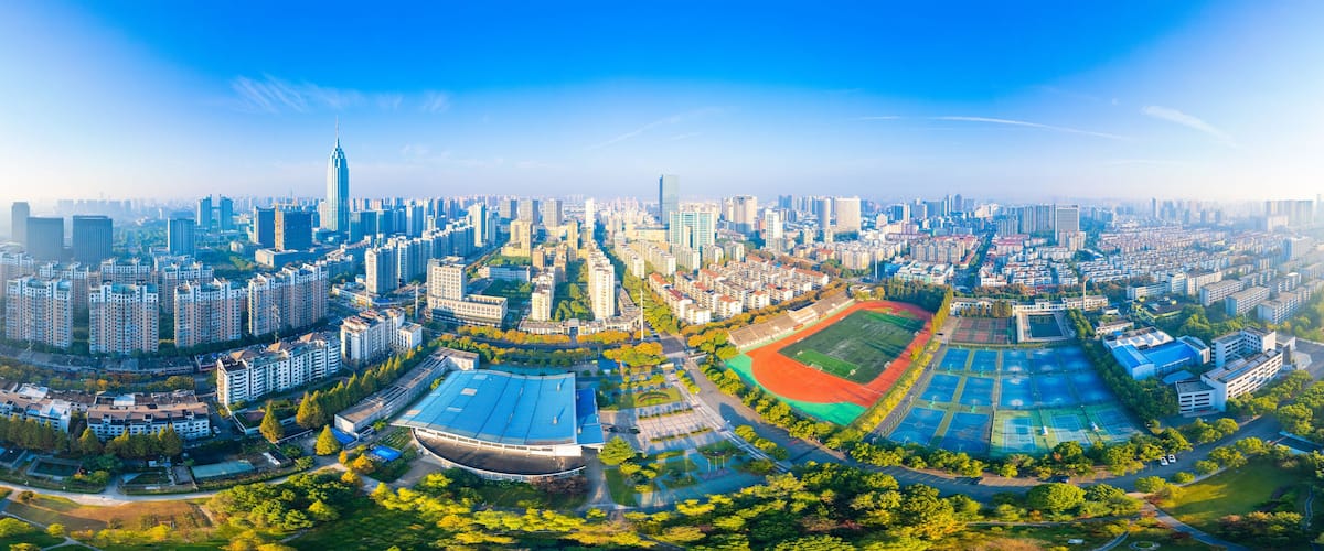 A panoramic view of a modern city with high-rise buildings, a prominent skyscraper, and a large sports complex.