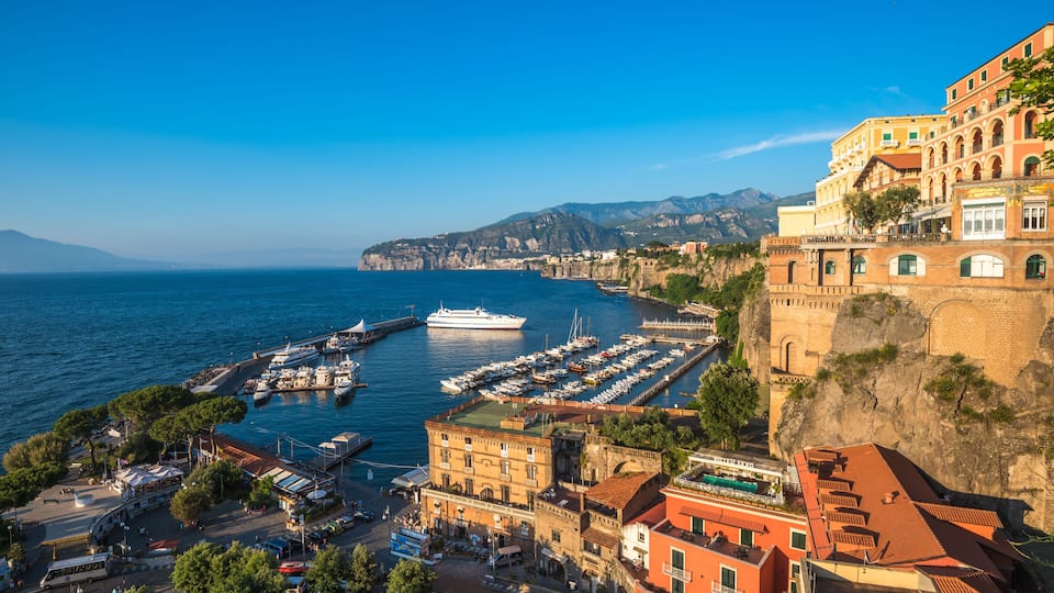 A coastal town with a marina, historic buildings, and a cliffside.