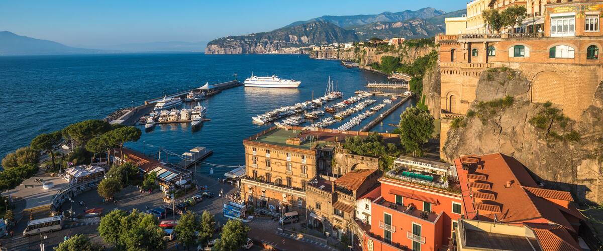 A coastal town with a marina, historic buildings, and a cliffside.