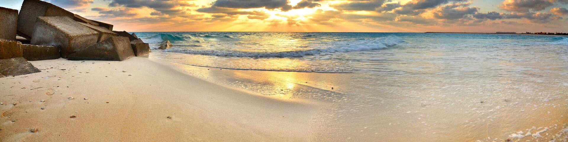 A beach with waves, a sunset, and a rocky outcrop.