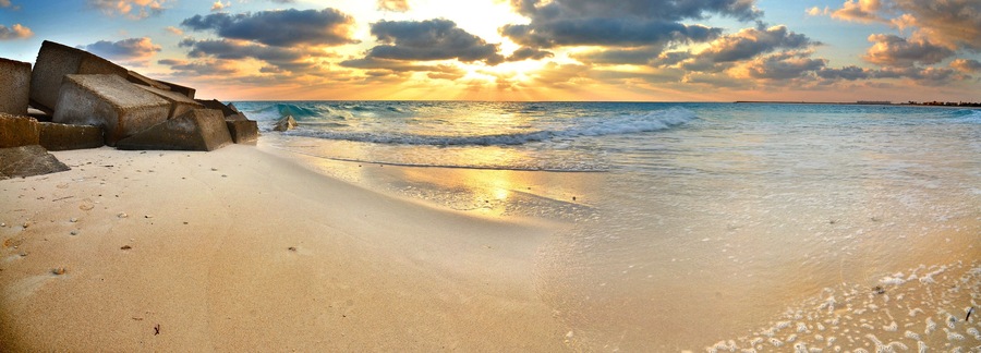 A beach with waves, a sunset, and a rocky outcrop.