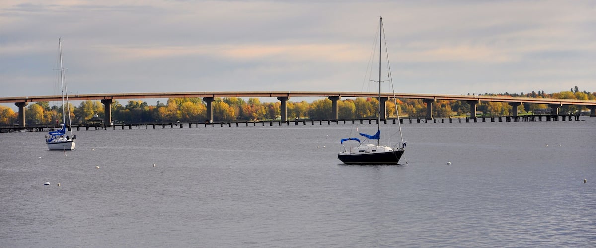 A calm river with sailboats and a bridge in the background.