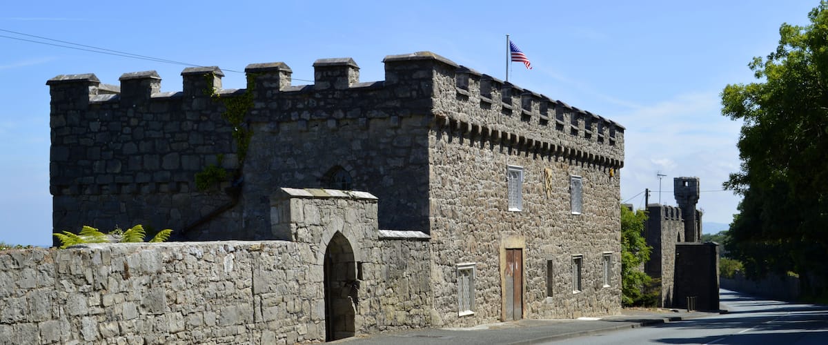 A stone castle with an American flag, a clear sky, and a road in front.
