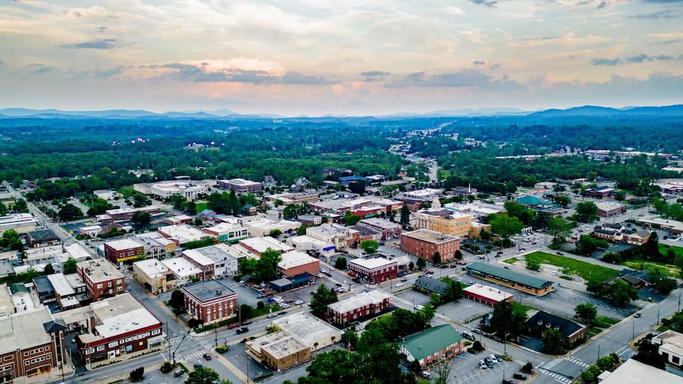 An aerial view of a town with a central square, surrounding buildings, and distant mountains.