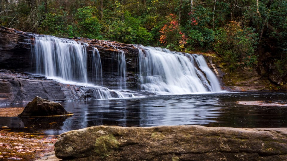 A waterfall cascading over rocks into a calm pool, surrounded by dense forest.