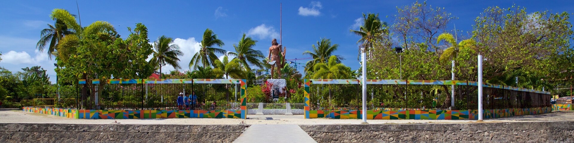 Una estatua en un parque con cercas coloridas y palmeras.