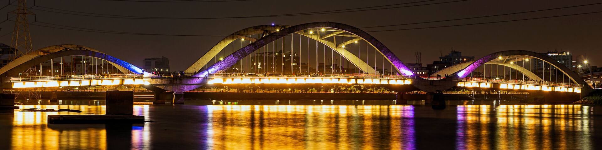 A brightly lit bridge with a reflective water surface at night.