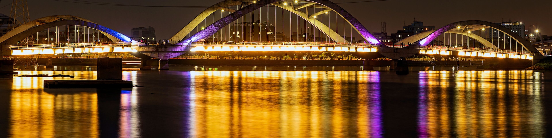 Uma ponte bem iluminada com superfície aquática refletindo à noite.