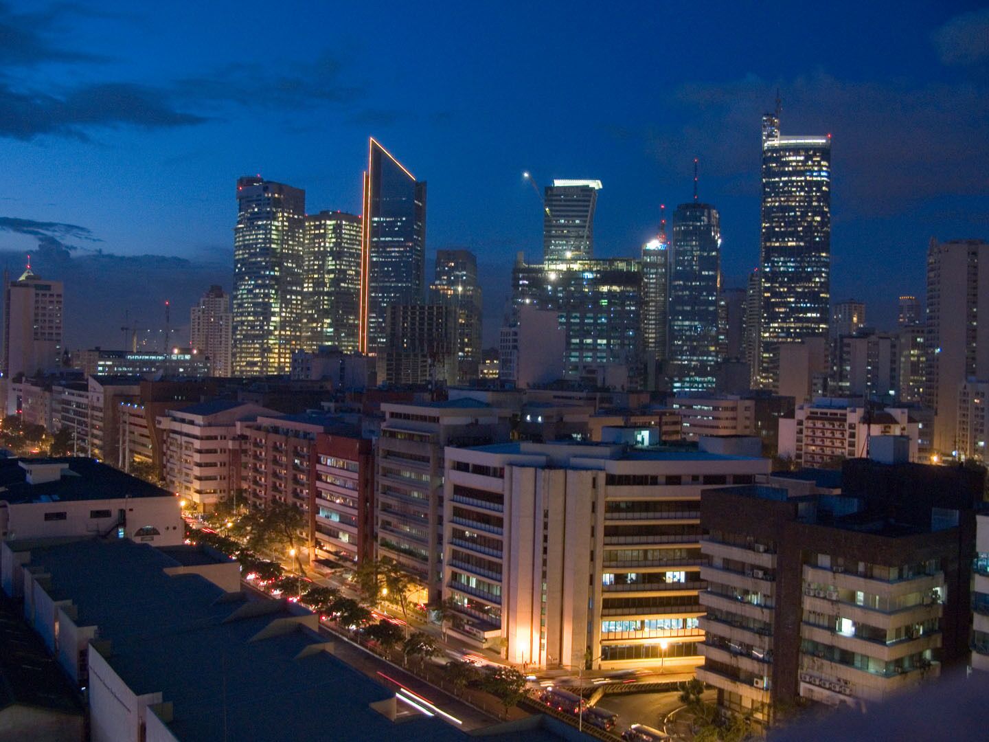 A city skyline at dusk with illuminated skyscrapers and a busy street.