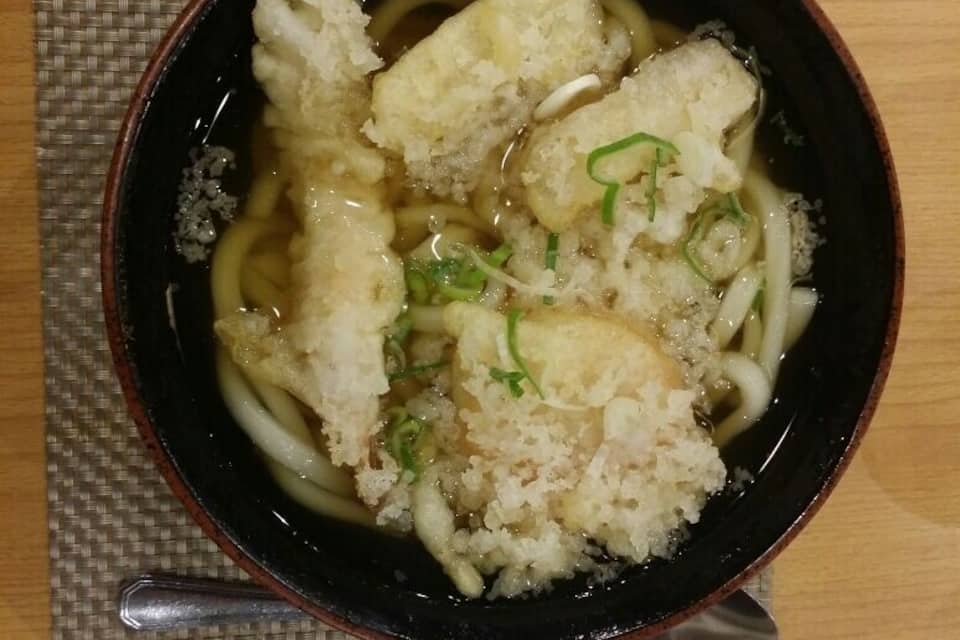 Uma tigela de ramen com macarrão, tofu e cebolinha sobre um descanso de tecido trançado.