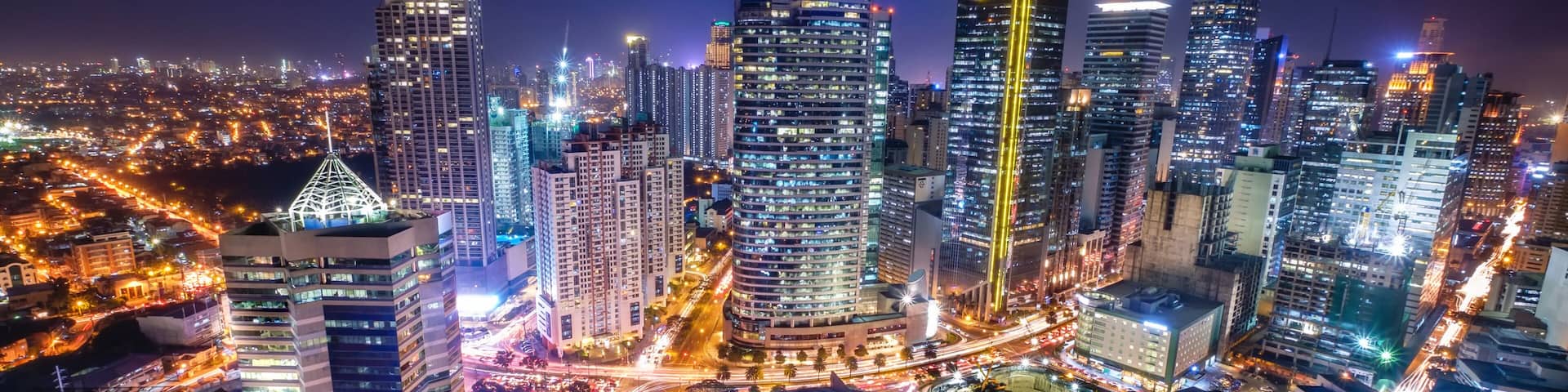 A cityscape at night with illuminated skyscrapers and a busy intersection.