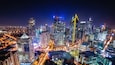 A cityscape at night with illuminated skyscrapers and a busy intersection.