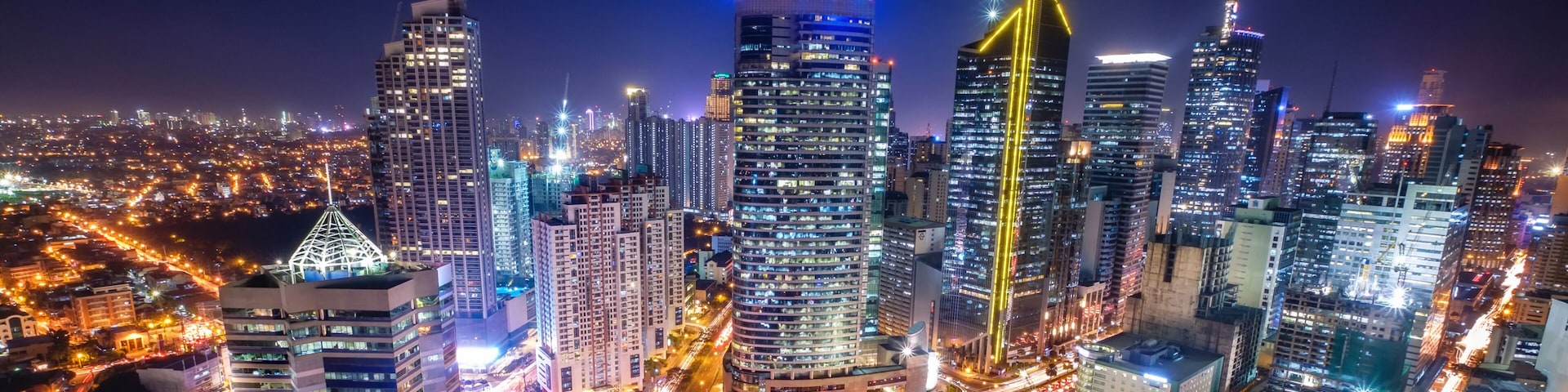 Paisagem urbana noturna com arranha-céus iluminados e um cruzamento movimentado.
