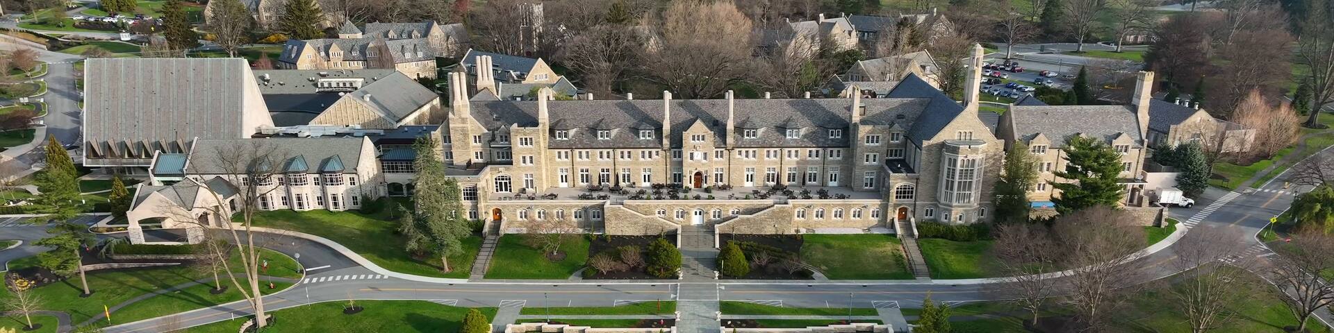 An aerial view of a large, historic building complex with symmetrical architecture, a central courtyard, and a pool.