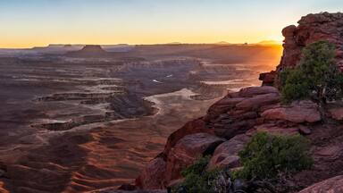 Un extenso paisaje cañonero con formaciones rocosas estratificadas y un atardecer al fondo.
