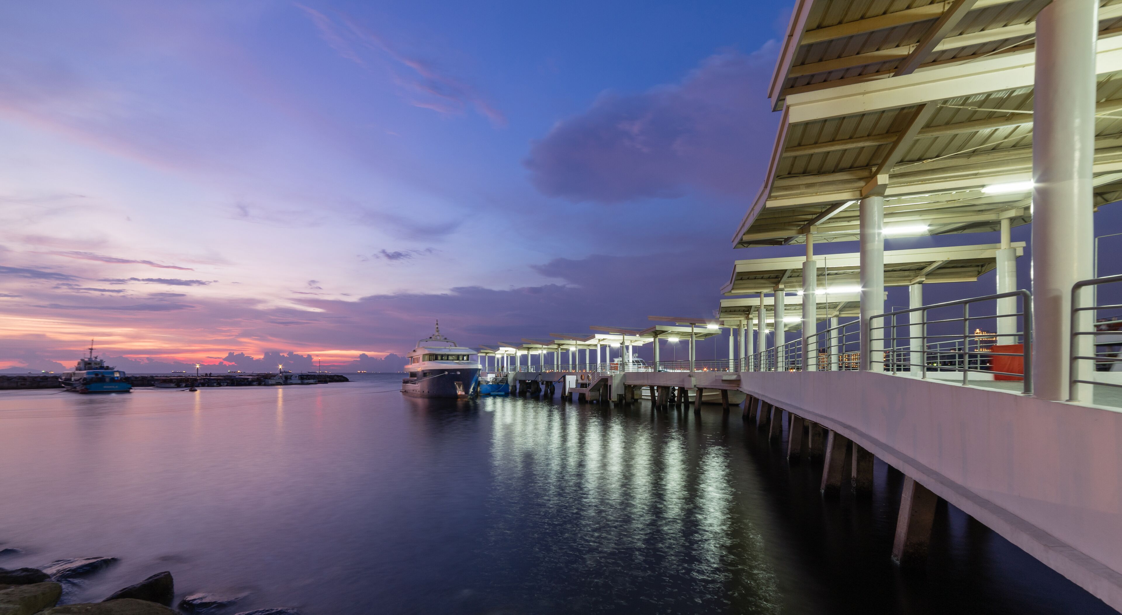 A waterfront pier with boats docked, a sunset, and a city skyline in the background.