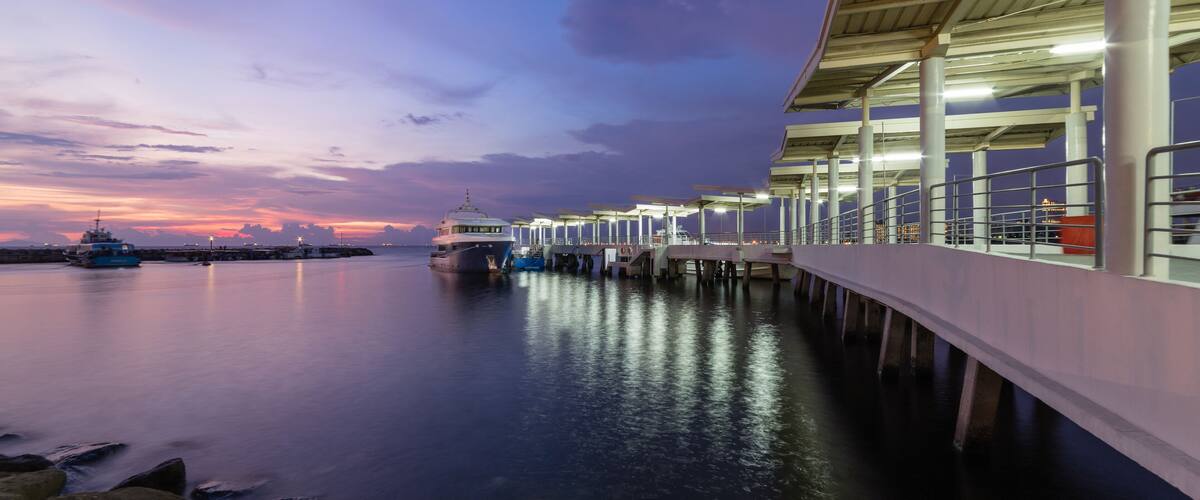 A waterfront pier with boats docked, a sunset, and a city skyline in the background.