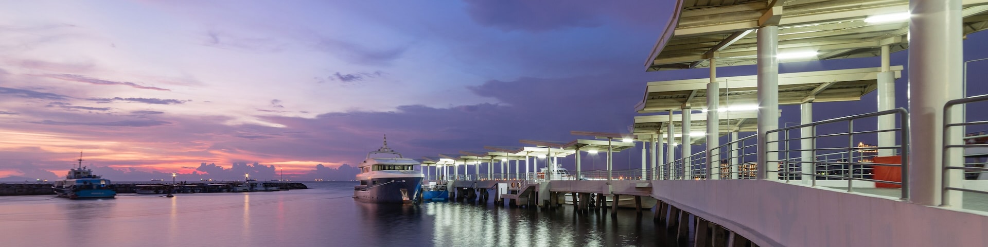 A waterfront pier with boats docked, a sunset, and a city skyline in the background.