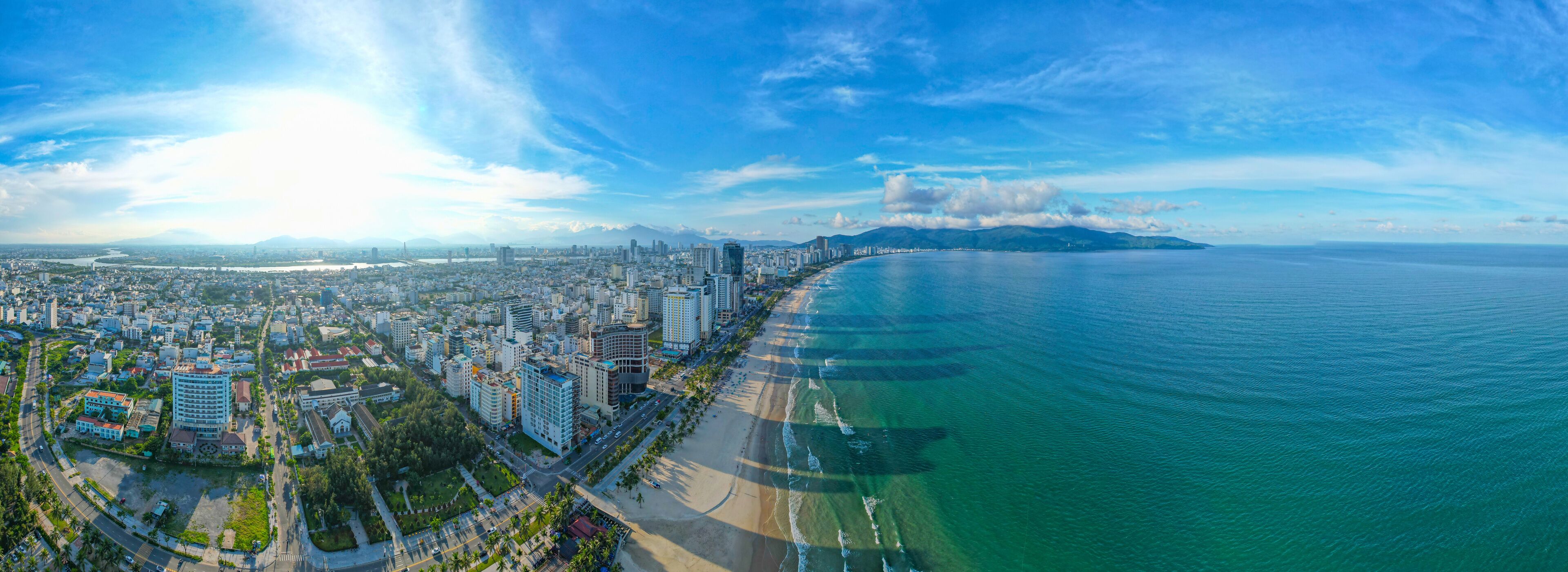 Un paysage urbain côtier avec une plage, des immeubles de grande hauteur et une chaîne de montagnes à l’horizon.