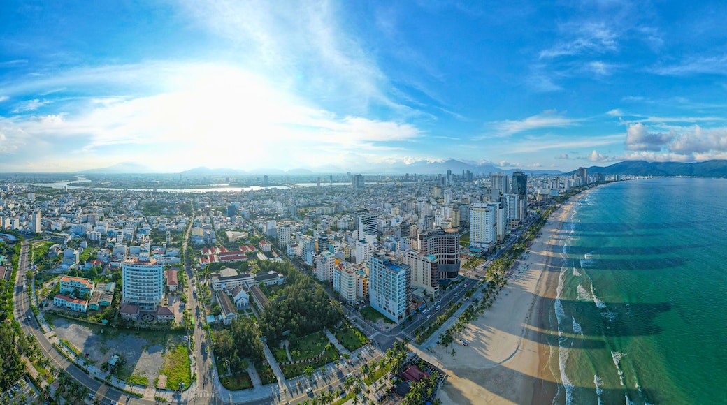 Un paysage urbain côtier avec une plage, des immeubles de grande hauteur et une chaîne de montagnes à l’horizon.