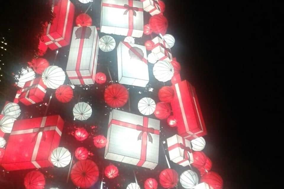 Un árbol de Navidad adornado con cajas de regalo rojas y blancas y farolillos rojos.