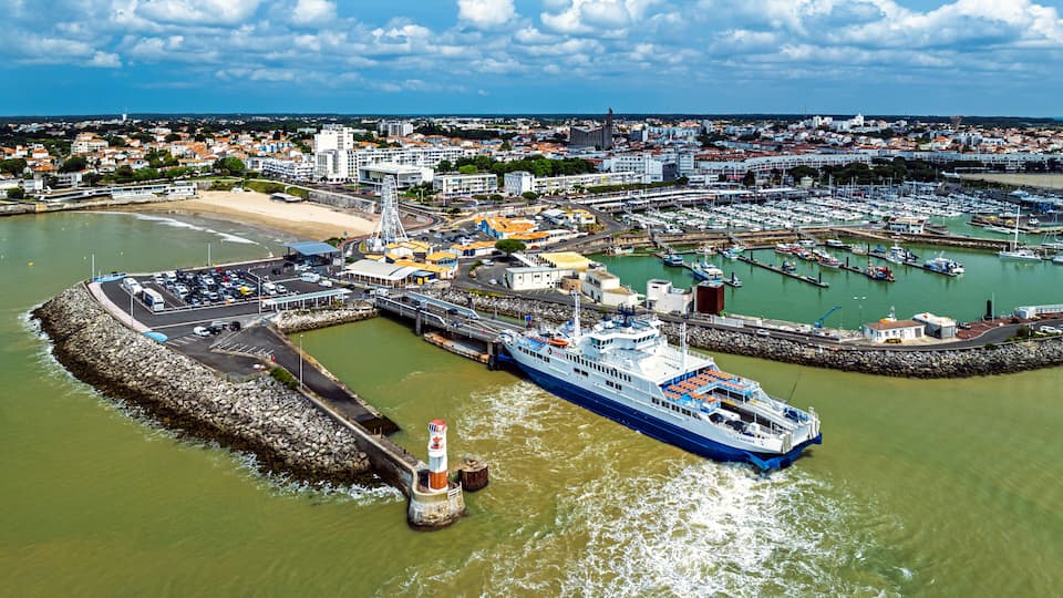 A coastal cityscape with a large ferry dock, a lighthouse, and a marina filled with boats.