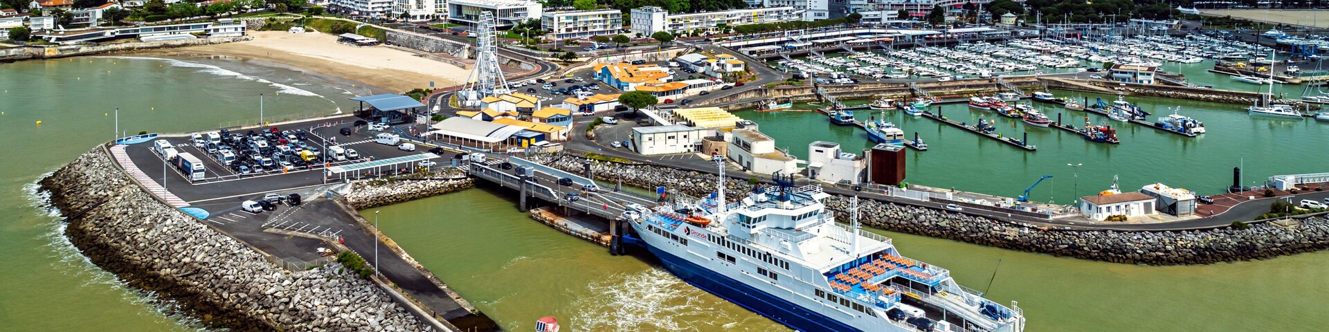 Un paisaje urbano costero con un muelle de transbordador grande, un faro y un puerto deportivo lleno de barcos.