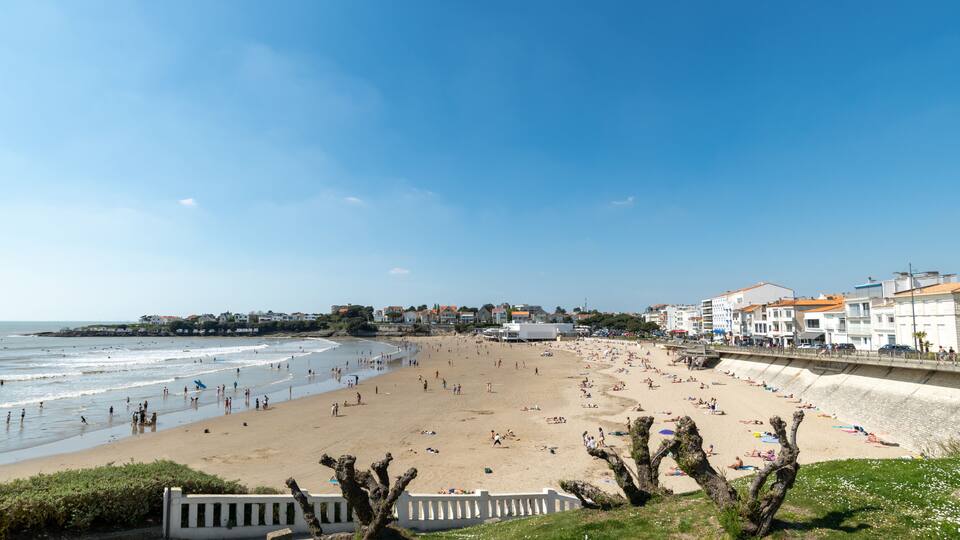 A coastal beach with people, a promenade, and buildings along the shore.