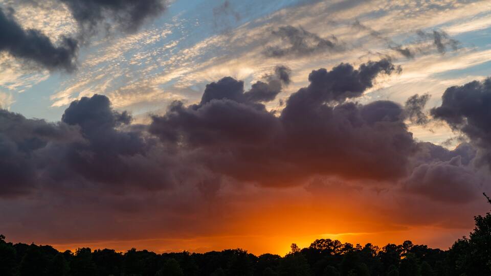 A sunset over a park with trees and a cloudy sky.