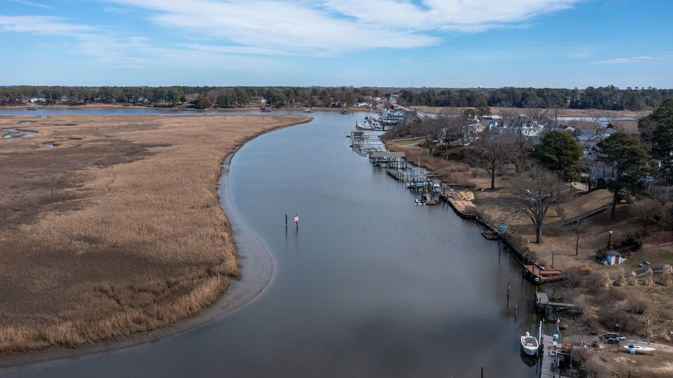 A river curving through a landscape with dry grass fields, a dock with boats, and houses along the riverbank.