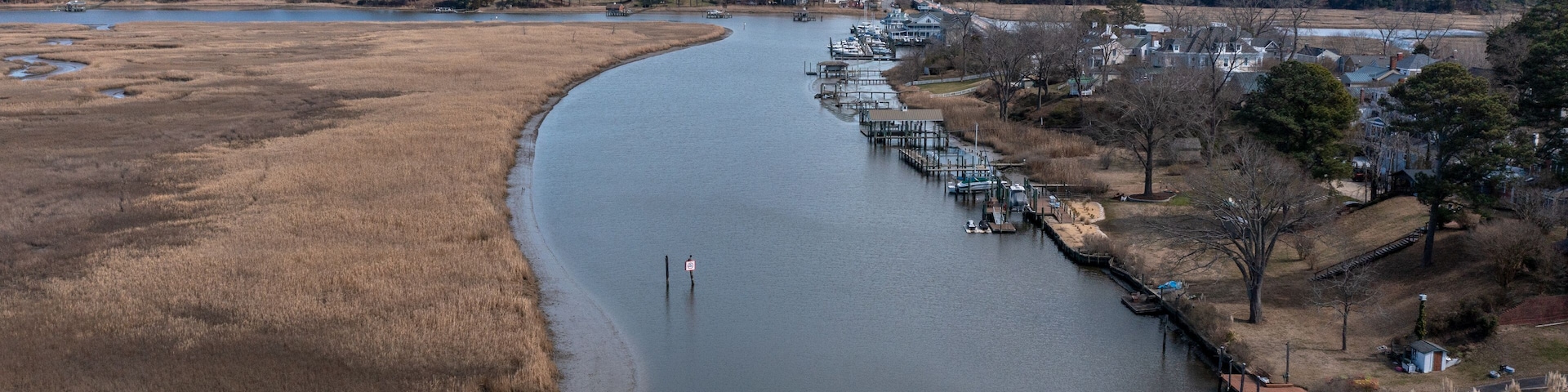 A river curving through a landscape with dry grass fields, a dock with boats, and houses along the riverbank.